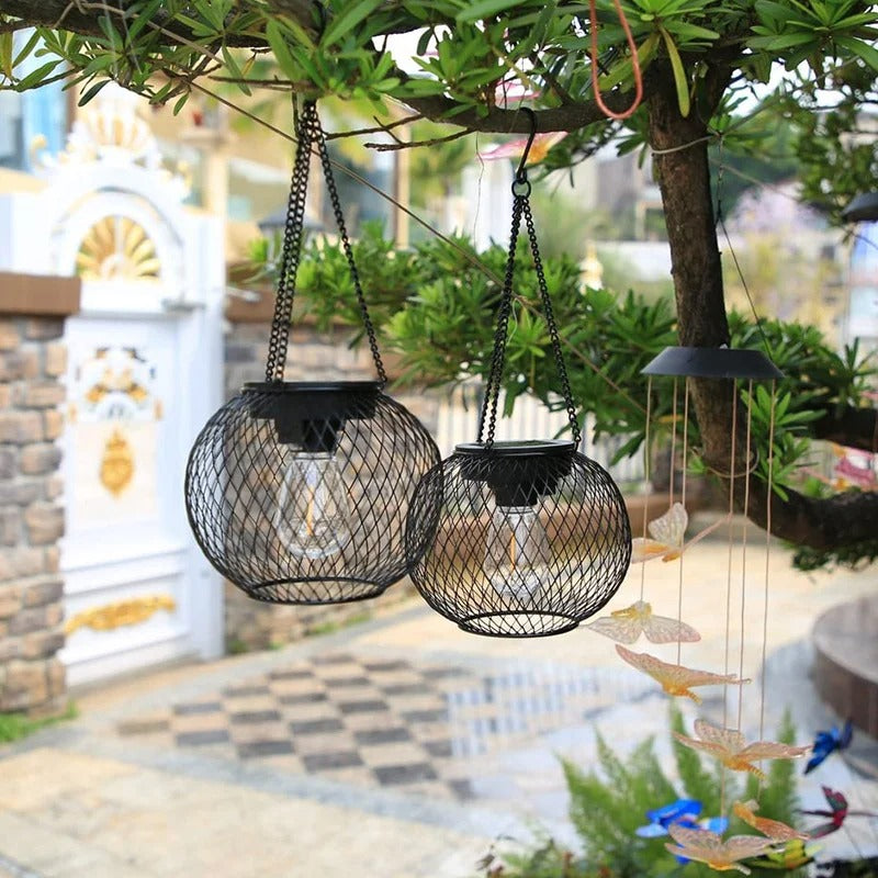 Deux lampe solaire jardin haut de gammeL'ambiance charme le jardin alors qu'ils pendent à une branche d'arbre parmi les feuilles vertes. Une décoration en forme de papillon est également accrochée à proximité, avec un portail blanc et un chemin pavé en arrière-plan.
Two Lanterne solaire suspendue | Ambiance charm the garden as they dangle from a tree branch among green leaves. A butterfly decoration also hangs nearby, with a white gate and cobblestone path in the background.