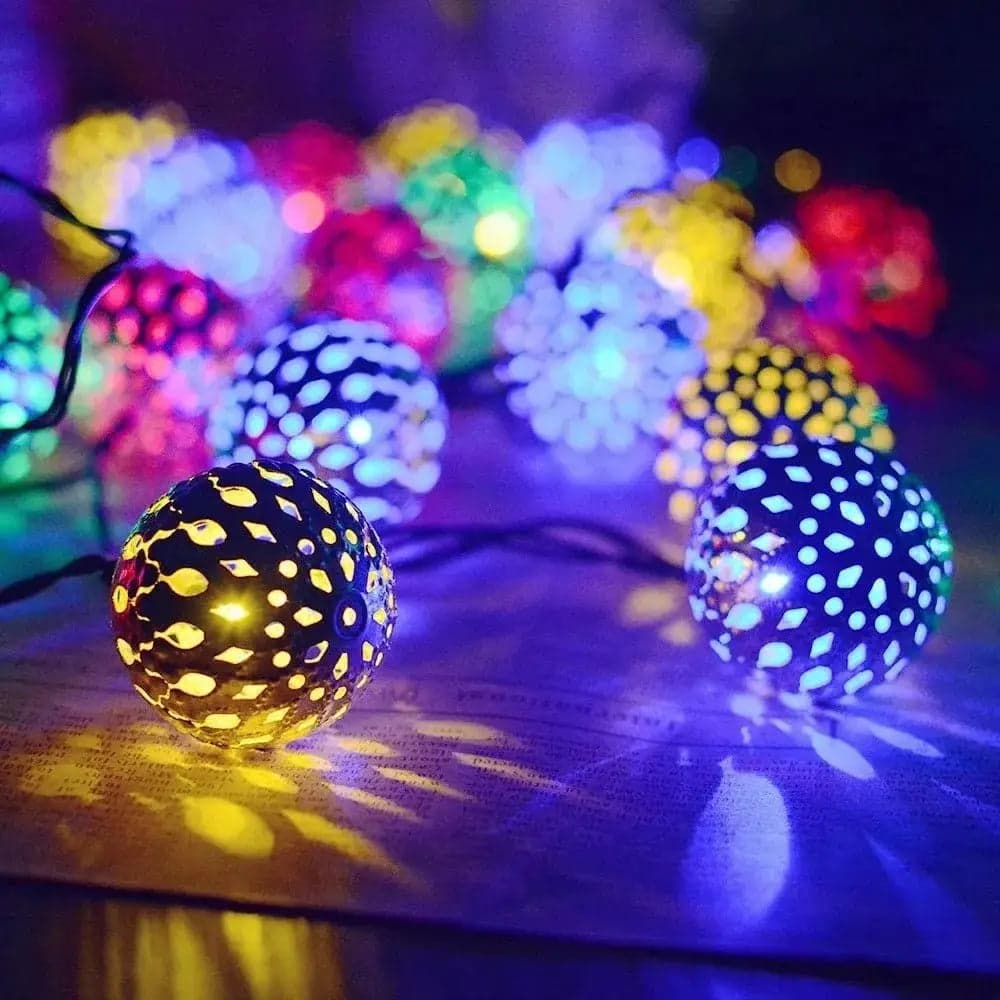 La Guirlande solaire | Cansol™ est composée de lumières décoratives sphériques aux motifs découpés complexes qui émettent des couleurs jaunes, bleues et rouges vibrantes. Disposées sur une surface, elles projettent des ombres colorées et créent une atmosphère festive.