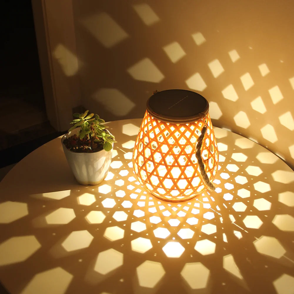 La Lampe solaire de jardin haut de gamme-Bambou Tissé diffuse des motifs géométriques raffinés sur une table ronde, accompagnée d'une petite plante en pot, créant une ambiance élégante et écologique sur un mur subtilement éclairé.