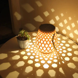 La Lampe solaire de jardin haut de gamme-Bambou Tissé diffuse des motifs géométriques raffinés sur une table ronde, accompagnée d'une petite plante en pot, créant une ambiance élégante et écologique sur un mur subtilement éclairé.