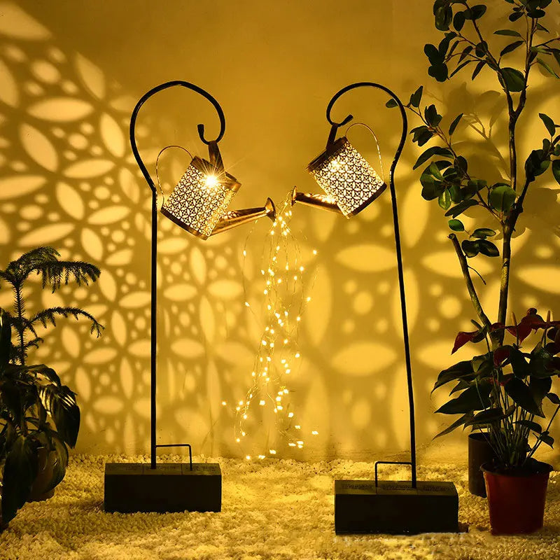 La Lampe solaire pour le jardin-Arrosoir est suspendue sur un support métallique incurvé, projetant une lumiÚre chaude et aquatique sur vos plantes. Cette élégante décoration extérieure crée des ombres ornées et une ambiance magique dans votre jardin.