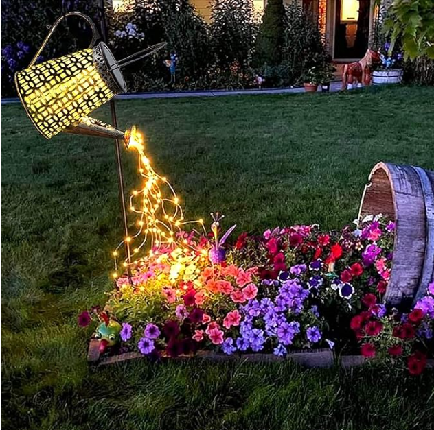 La Lampe solaire pour le jardin-Arrosoir illumine un massif de fleurs de ses lumiÚres scintillantes, ajoutant une touche féerique à votre extérieur au crépuscule, prÚs d'un demi-tonneau fleuri.