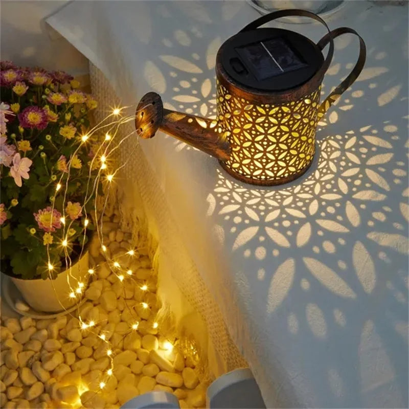 Lampe solaire pour le jardin-Arrosoir projette de jolis motifs floraux sur une surface blanche tandis que des guirlandes descendant de son bec, illuminant galets et fleurs en pot pour une superbe décoration extérieure.