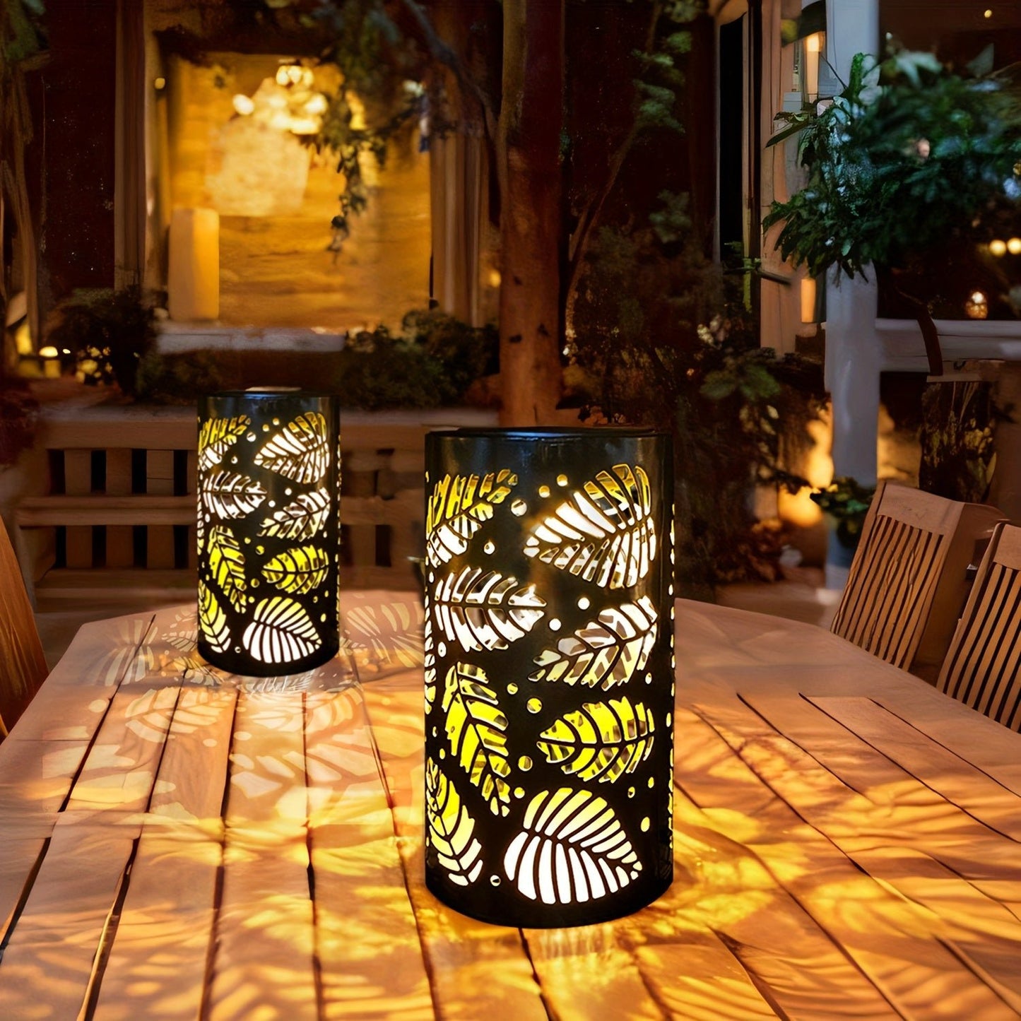Deux lanternes solaires extérieures à motif de feuilles illuminent une table en bois.