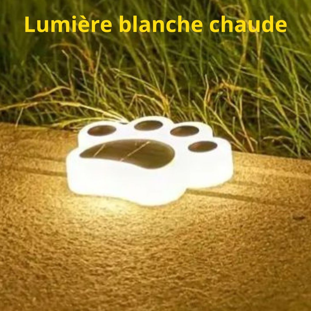 La lampe solaire de jardin Griffe de Chat, un luminaire blanc en forme de patte, repose sur du bois avec de lherbe à proximité. Le texte français Lumière blanche chaude suggère quelle est idéale pour léclairage extérieur.