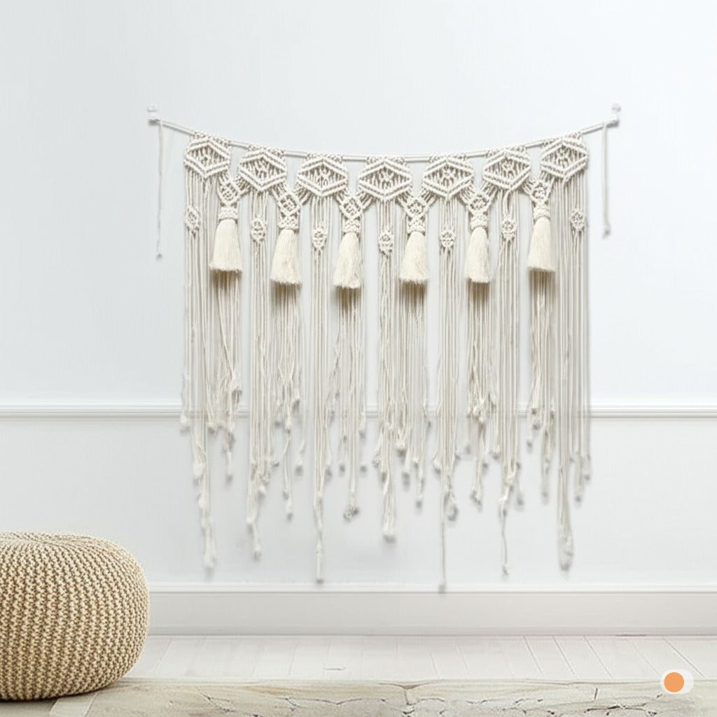 Rideau macramé décoratif en coton beige.
Design bohème avec des motifs géométriques et des franges.
Suspendu sur un mur blanc, ajoutant une touche artisanale et chaleureuse.
Présenté dans un intérieur épuré avec un pouf en rotin et un sol clair.