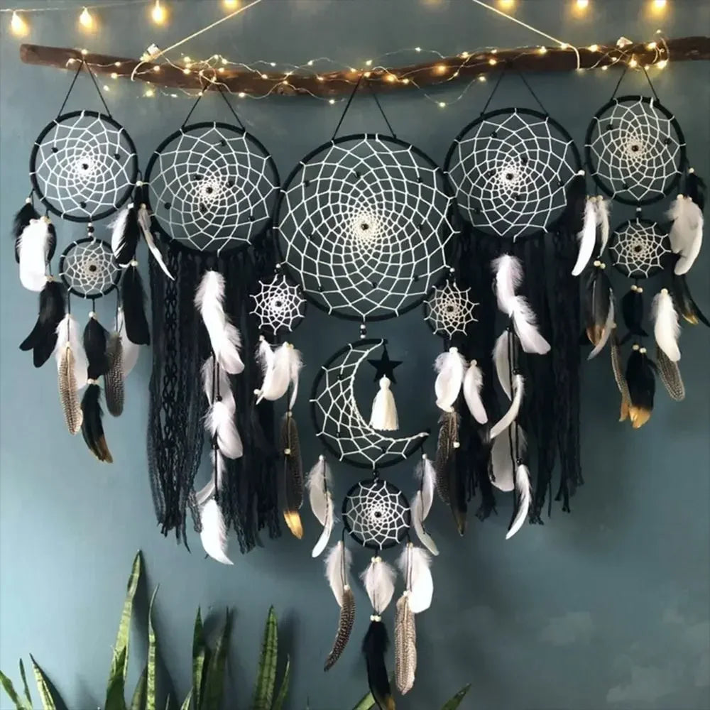 Un arrangement décoratif de plusieurs attrape-rêves suspendus à une branche. Les cercles sont ornés de motifs complexes évoquant le macramé, avec des fils blancs tissés en des toiles d'araignée délicates. Des plumes noires e Les cercles sont ornés de motifs complexes évoquant le macramé, avec des fils blancs tissés en des toiles d'araignée délicates. Des plumes noires et blanches pendent gracieusement, ajoutant une touche bohème. Une guirlande lumineuse diffuse une lumière douce sur cette décoration murale.