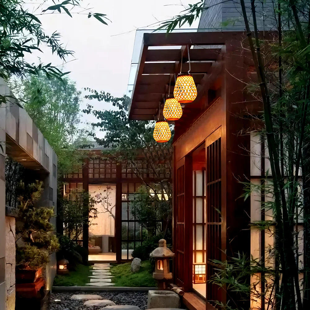 Un paisible jardin japonais est agrémenté d'un chemin de pierre, de bambous et de lanternes avec une Lampe solaire de jardin haut de gamme en bambou tissé pour un éclairage écologique. Une maison en bois avec des paravents shoji et des suspensions sublime la sérénité du soir.