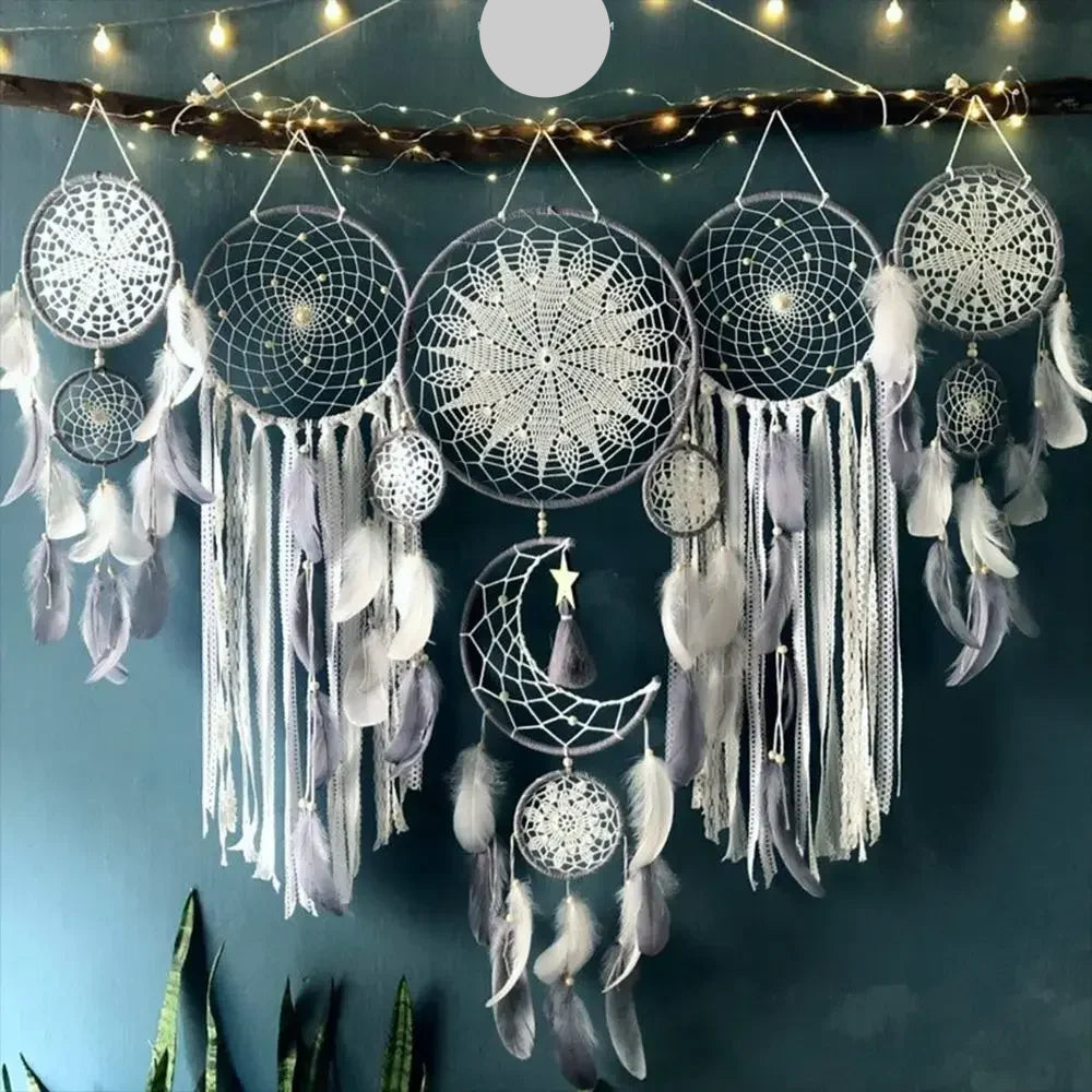 Une tenture murale décorative en macramé faite à la main orne un mur bleu foncé. Plusieurs attrape-rêves de différentes tailles, certains avec des motifs complexes en macramé au centre et d'autres avec des crochets délicats, pendent d'une branche. Des plumes douces et des cordes de macramé aux tons neutres ajoutent une touche bohème et artisanale à la pièce.