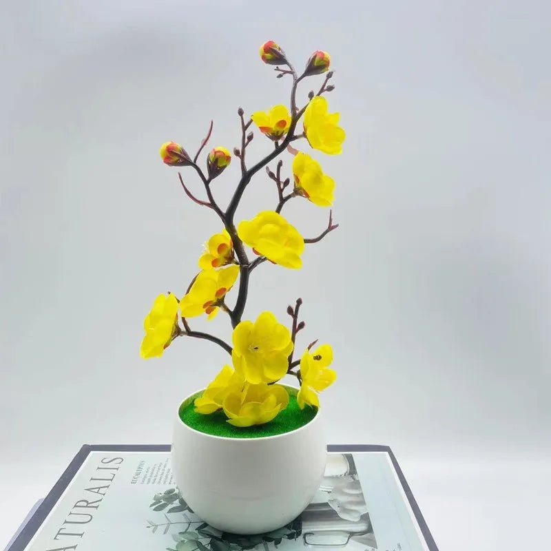 Plante artificielle fleurie jaune en pot blanc sur livre. Décoration intérieure.