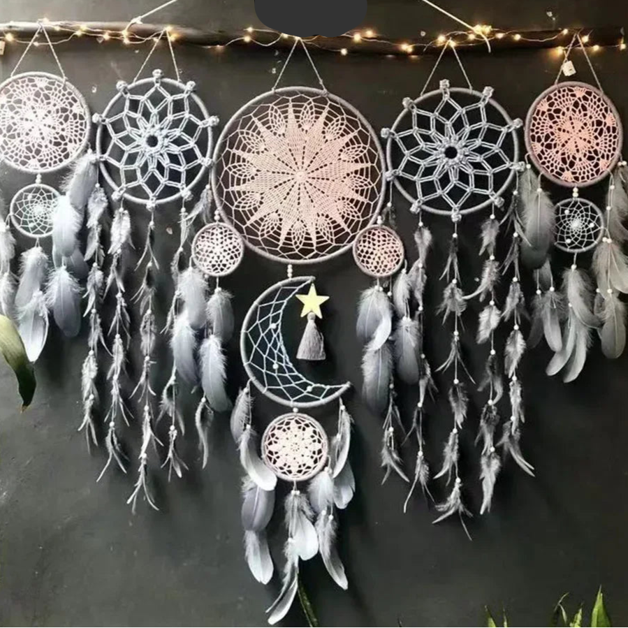 Décoration murale de style bohème, confectionnée en macramé. Plusieurs attrape-rêves de tailles variées, aux motifs délicats, sont suspendus à une branche ornée de petites lumières. Des plumes douces et vaporeuses pendent de chaque cercle, ajoutant une touche de légèreté et de rêve à l'ensemble.