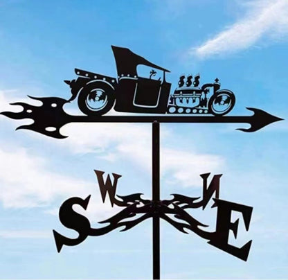 La silhouette d'une "Girouette de jardin-Galion", représentant une voiture ancienne avec des flammes, pointe vers le nord. Les directions cardinales (S, W, E, N) sont visibles en dessous sur un ciel bleu clair, une pièce de décoration extérieure idéale.