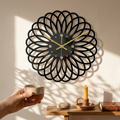 Vue de face horloge noire moderne motif floral — cadran sans chiffres, aiguilles dorées, style industriel.