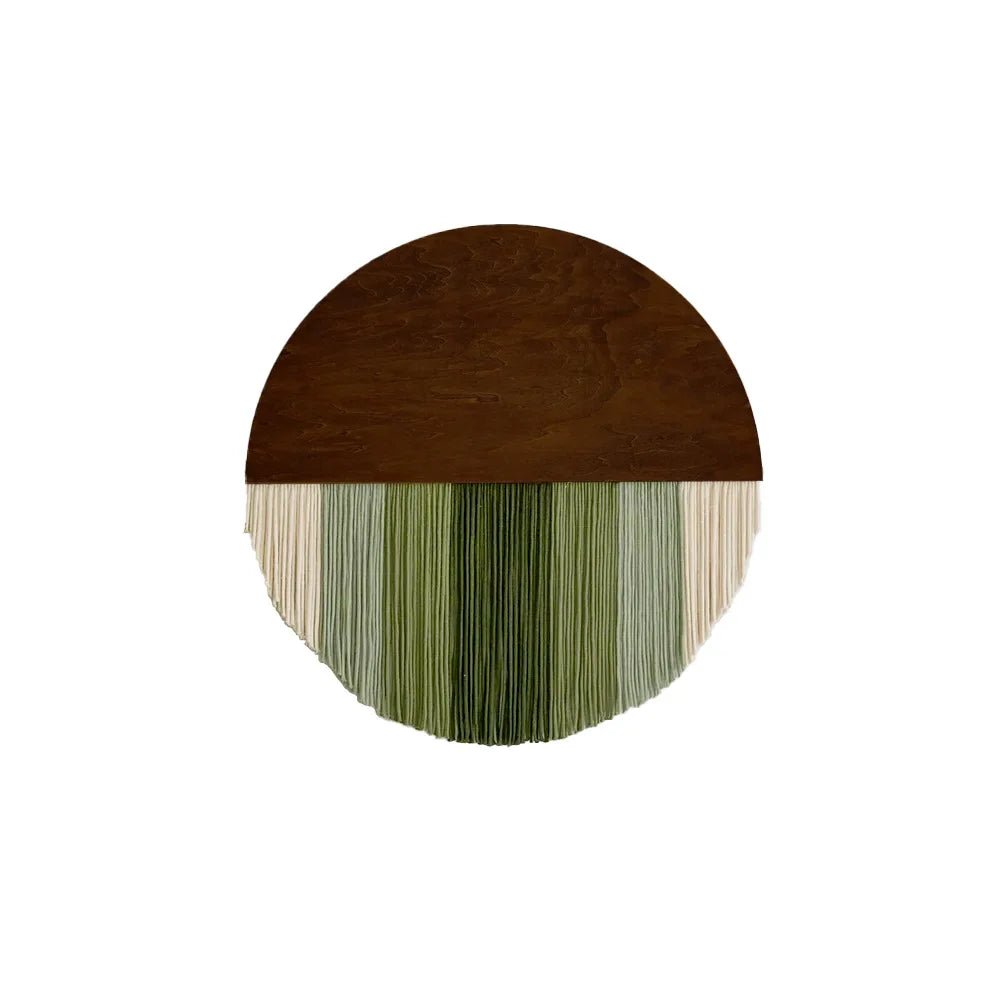Décoration murale en macramé présentant un demi-cercle en bois brun sur le dessus. De fines cordes pendantes en coton dans des tons crème et différentes nuances de vert créent une texture douce et un motif rayé. Cet article artisanal apportera une touche naturelle et bohème à votre intérieur.