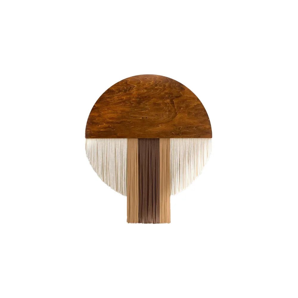 Décoration murale en macramé présentant un demi-cercle supérieur en bois brun avec des veinures apparentes. Des franges de fils de coton de différentes couleurs (blanc cassé, beige clair, marron clair et marron foncé) pendent du bois, formant un motif vertical central plus dense. L'ensemble crée une pièce artisanale texturée et naturelle.