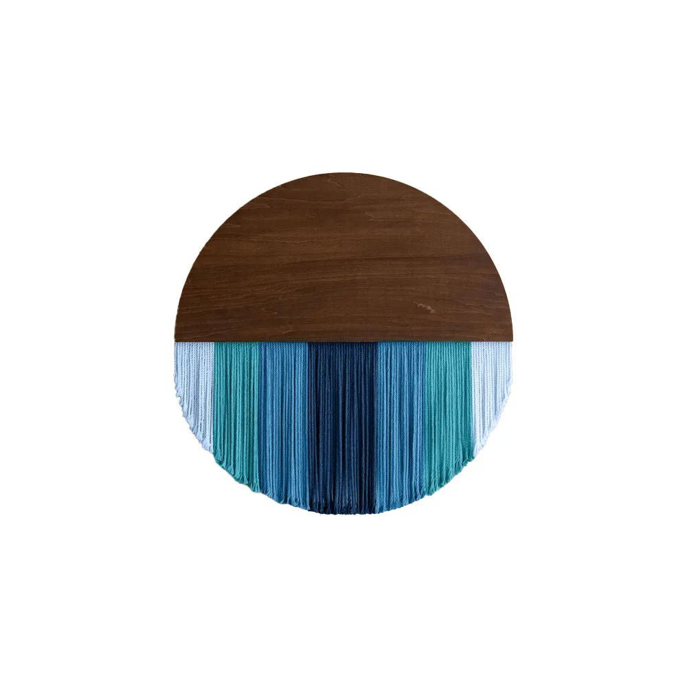 Décoration murale en macramé présentant un demi-cercle supérieur en bois brun lisse, contrastant avec une cascade de fils de coton dans des tons de bleu et de turquoise. Les franges créent un effet visuel apaisant et texturé. Cet artisanat unique apporte une touche bohème et élégante à tout intérieur.