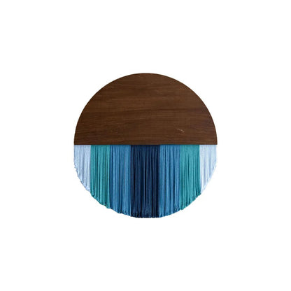 Décoration murale en macramé présentant un demi-cercle supérieur en bois brun lisse, contrastant avec une cascade de fils de coton dans des tons de bleu et de turquoise. Les franges créent un effet visuel apaisant et texturé. Cet artisanat unique apporte une touche bohème et élégante à tout intérieur.