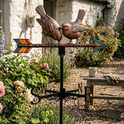 Détail d'une Girouette oiseau décorative avec deux oiseaux sur une flèche, installée sur un mât en fer forgé dans un jardin rustique.