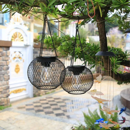 Deux Lanterne solaire suspendue | L'ambiance charme le jardin alors qu'ils pendent à une branche d'arbre parmi les feuilles vertes. Une décoration en forme de papillon est également accrochée à proximité, avec un portail blanc et un chemin pavé en arrière-plan.
Two Lanterne solaire suspendue | Ambiance charm the garden as they dangle from a tree branch among green leaves. A butterfly decoration also hangs nearby, with a white gate and cobblestone path in the background.
