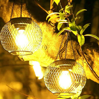 Deux Lanterne solaire suspendue | Ambiance avec des lumières jaunes chaudes suspendues à une branche d'arbre. Leur conception en treillis métallique complète les feuilles vertes, offrant un éclairage extérieur élégant qui améliore l'ambiance chaleureuse du jardin.
Two Lanterne solaire suspendue | Ambiance with warm yellow lights hang from a tree branch. Their wire mesh design complements the green leaves, providing elegant éclairage extérieur that enhances the jardins cozy ambiance.