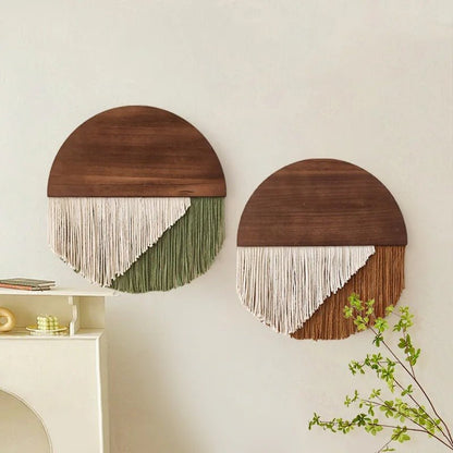 Deux décorations murales circulaires présentent une moitié supérieure en bois lisse de couleur noyer et une moitié inférieure en macramé. L'une combine des cordes blanches et vert olive, tandis que l'autre marie le blanc et une nuance chaude de terre cuite. Elles sont accrochées sur un mur blanc cassé, apportant une touche artisanale et naturelle à l'espace.
