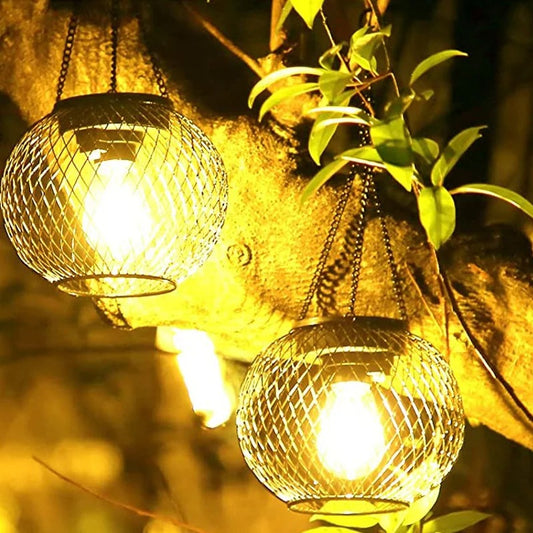 Deux lampe solaire jardin haut de gamme avec des lumières jaunes chaudes suspendues à une branche d'arbre. Leur conception en treillis métallique complète les feuilles vertes, offrant un éclairage extérieur élégant qui améliore l'ambiance chaleureuse du jardin.
Two Lanterne solaire suspendue | Ambiance with warm yellow lights hang from a tree branch. Their wire mesh design complements the green leaves, providing elegant éclairage extérieur that enhances the jardins cozy ambiance.