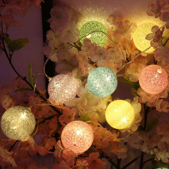 Guirlande lumineuse colorée, boules tissées, ambiance douce sur fleurs.