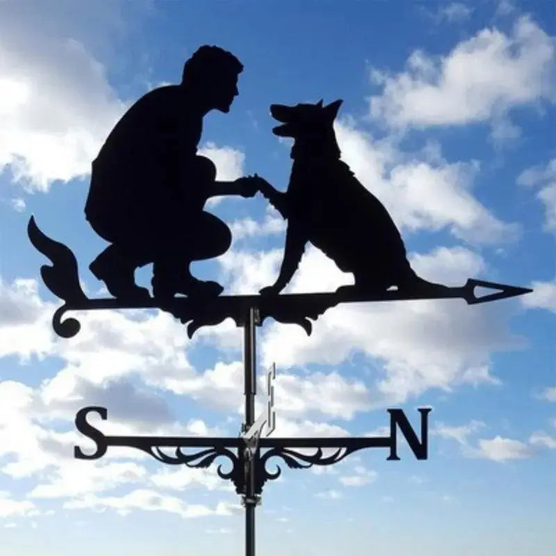 Girouette animal en fer forgé noir représentant un chien et son maître au-dessus des points cardinaux sous un ciel bleu.