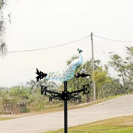 Girouette oiseau paon sur fond de jardin verdoyant et allée.
