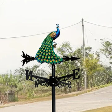 Girouette oiseau paon décorative, jardin verdoyant, ciel nuageux.