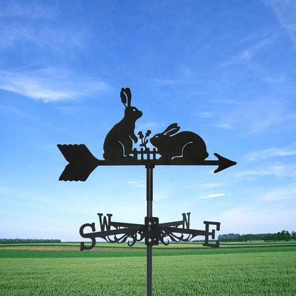 La silhouette de deux lapins sur une girouette en acier tourne élégamment en flèche sur le ciel bleu au-dessus d'un champ verdoyant. Conçue comme une charmante « Girouette animal-Dragon volant », elle représente les points cardinaux (S, O, N, E) sous les lapins.