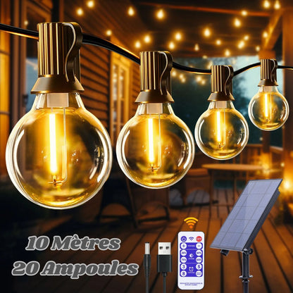 La Guirlande solaire extérieure puissante | Ambiance Enchantée diffuse une lueur chaleureuse avec des ampoules rondes pour une ambiance magique sur une véranda en bois. Limage présente un emballage « 10 mètres, 20 ampoules », ainsi quune télécommande et un panneau solaire pour la fonctionnalité de guirlande lumineuse solaire.
