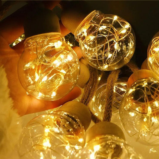 Gros plan sur une Guirlandes solaire extérieur  ronde avec des ampoules chaudes et lumineuses. Les ampoules contiennent des fils fins et entrelacés émettant une lumière dorée, créant une ambiance chaleureuse et festive. Une main tient une ampoule, ce qui renforce léclairage chaleureux.