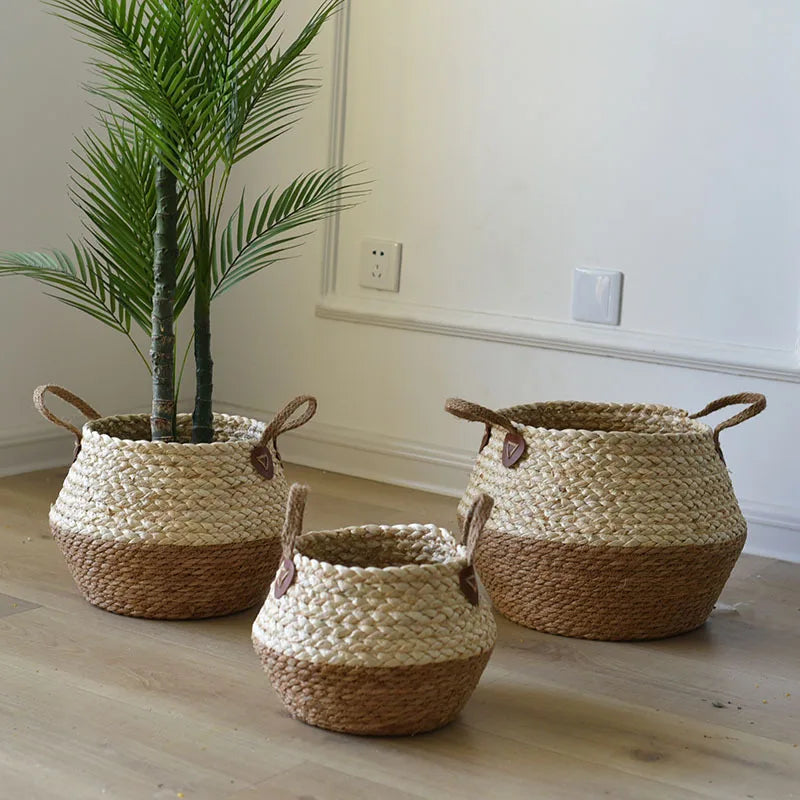 Cache-pot en rotin ventre arrondi coloris écru avec anses, posé sur parquet avec palmier artificiel