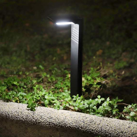 La Lampe solaire extérieur | Écolo est un éclairage de chemin moderne qui projette une lumière blanche éclatante sur les bordures de jardin, mettant en valeur les paysages de manière économique. Son design noir élégant contraste magnifiquement avec la verdure et les textures de pierre, offrant une solution déclairage écologique et sans effort.