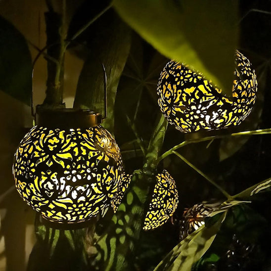 La lanterne solaire extérieure de Mafrenesiedecoration combine des motifs floraux complexes et une lueur alimentée par lénergie solaire, nichée au milieu dune verdure luxuriante pour créer une ambiance sereine, idéale pour léclairage extérieur décoratif.