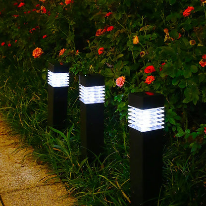 Trois lampes de jardin illuminées bordent une allée bordée de verdure et de fleurs rouges et roses éclatantes. Le design épuré et moderne des lampes contraste avec le feuillage luxuriant, créant une ambiance extérieure accueillante.