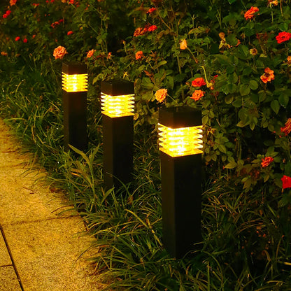 Trois lampadaires extérieurs noirs au design moderne émettent une lueur jaune chaude, illuminant un chemin de jardin bordé dune verdure luxuriante et de fleurs rouges et orange vibrantes.