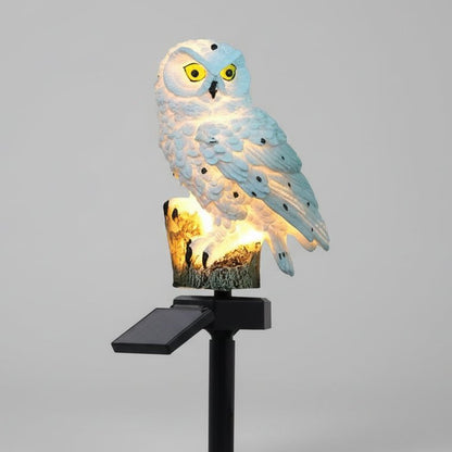Lampe solaire extérieur hibou en résine blanche éclairée la nuit dans un jardin, lumière LED chaleureuse automatique.