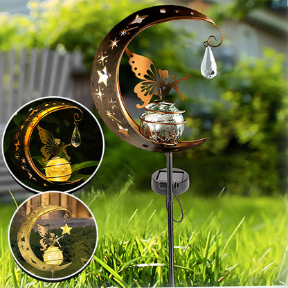 La Lampe solaire jardin haut de gamme forme de lune de Mafrenesiedecoration, ou LunaGlow, présente un motif découpé en forme de lune et de papillon. Elle contient un globe en verre avec des cristaux suspendus et des étoiles sur un piquet noir, créant une lumière magique la nuit comme le montrent les images lumineuses en médaillon.