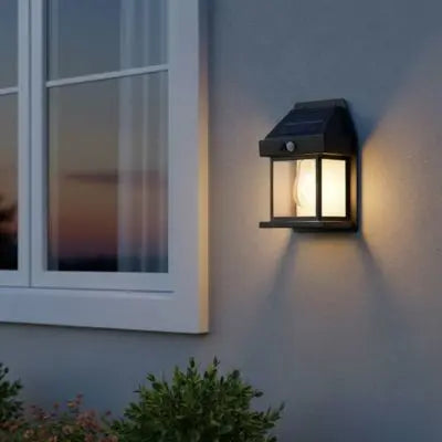 Lampe solaire jardin haut de gamme installée sur une façade moderne gris bleu, diffusant une lumière chaude à la tombée de la nuit.