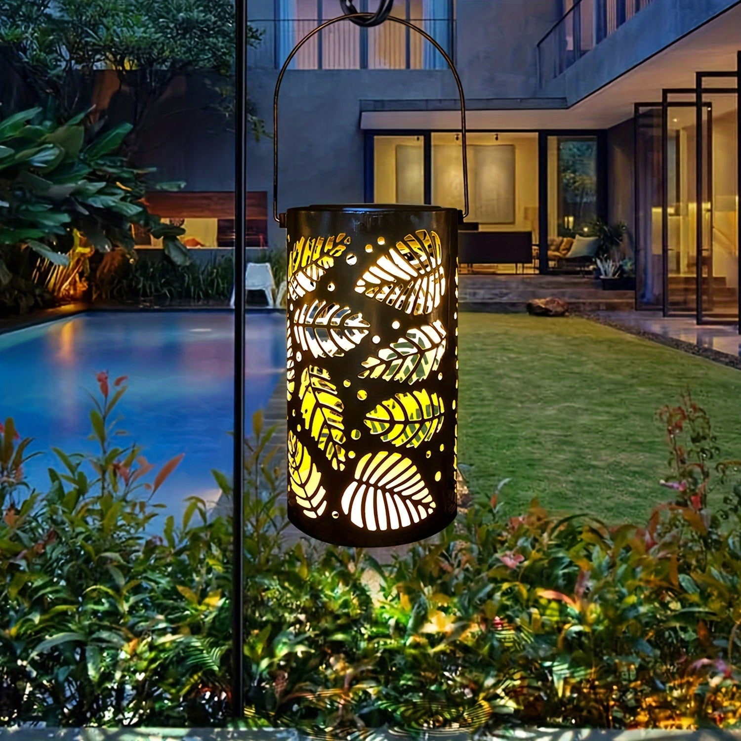 Lanterne solaire exterieur : Lanterne décorative à motif de feuilles éclairant un jardin près d'une piscine au crépuscule.
