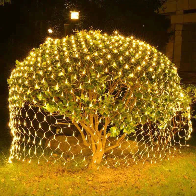  Guirlande rideau solaire lumineuse en forme de filet illuminant un arbuste la nuit.