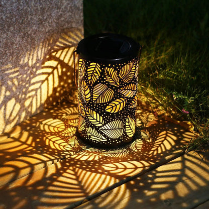 Lanterne solaire décorative projetant des ombres de feuilles sur terrasse en bois.