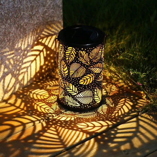 Lanterne solaire décorative projetant des ombres de feuilles sur terrasse en bois.