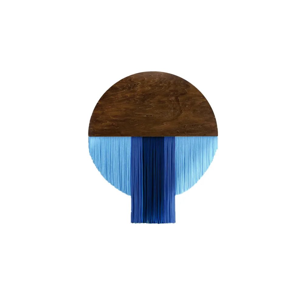 Macramé décoratif mural présentant un demi-cercle supérieur en bois brun lisse, surmonté d'une frange de fils de coton bleus de différentes nuances, créant un contraste moderne et texturé. La pièce artisanale évoque un style bohème chic.