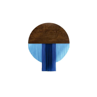 Macramé décoratif mural présentant un demi-cercle supérieur en bois brun lisse, surmonté d'une frange de fils de coton bleus de différentes nuances, créant un contraste moderne et texturé. La pièce artisanale évoque un style bohème chic.