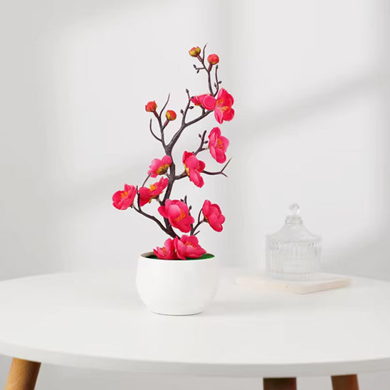 Une élégante Plante artificielle avec des fleurs roses vives dans un pot blanc.