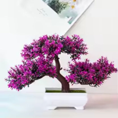 Sur cette image, on aperçoit une jolie plante artificielle en forme de bonsaï. Ses feuilles d'un violet éclatant apportent une touche de couleur vive. Elle est disposée dans un pot blanc carré et repose sur une surface claire. Un fond blanc avec un élément décoratif flou complète la scène. Cette plante artificielle est un bel ajout décoratif.