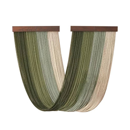 Rideaux décoratifs en macramé suspendus à deux supports en bois foncé. Les fils vert sauge, vert olive et beige crème créent un motif rayé vertical ondulant doucement vers le bas. L'artisanat délicat et les tons naturels apportent une touche bohème et élégante à la décoration intérieure.